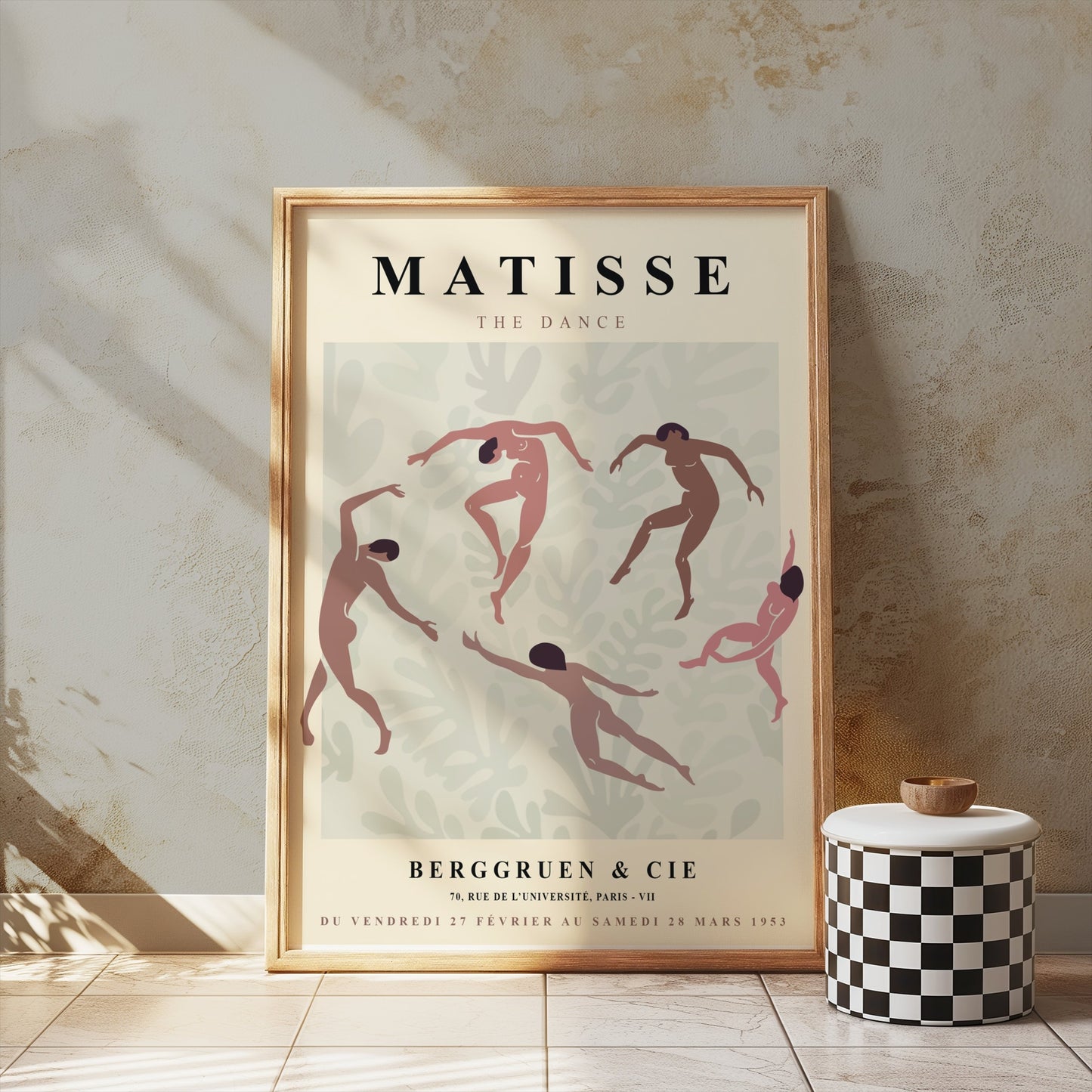 Matisse The Dance exhibition poster in a wooden frame leaning against a textured wall, styled with a checkered stool and soft lighting.