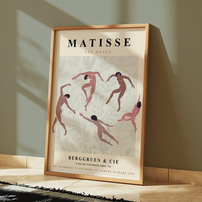 Matisse The Dance exhibition poster in a wooden frame leaning against a wall with warm lighting and a minimalist rug.