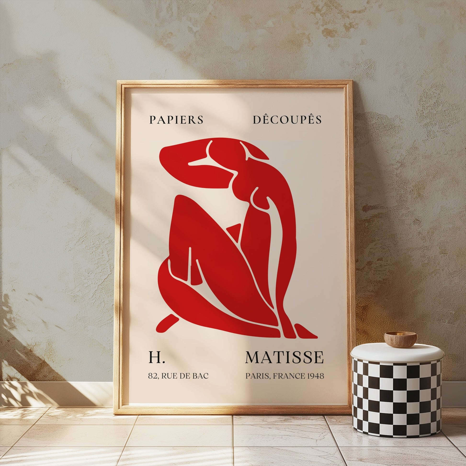 Henri Matisse 'Papiers Découpés' poster in a wooden frame, leaning against a textured wall, showcasing red abstract art for home decor.