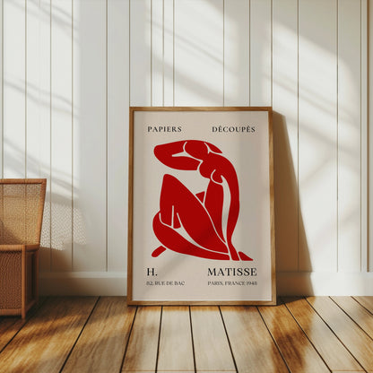 Framed Henri Matisse 'Papiers Découpés' poster with red abstract figure art, leaning against a white paneled wall for modern decor.