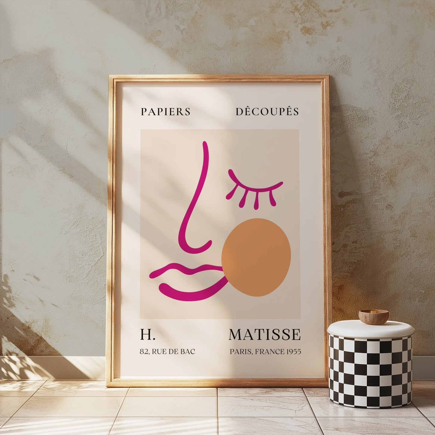 Abstract face art inspired by Matisse posters in a wooden frame, leaning against a textured wall with soft natural lighting.