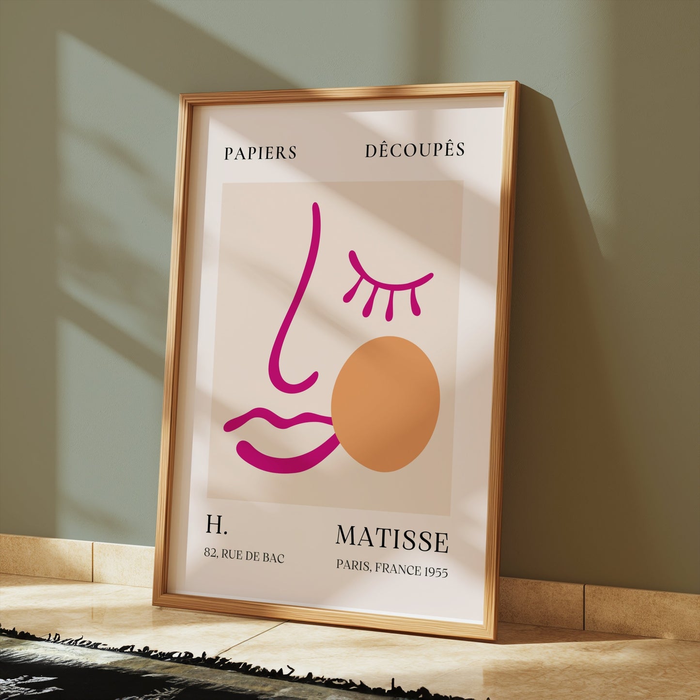 Abstract face art inspired by Matisse posters in a wooden frame, displayed on a tiled floor with soft sunlight streaming in.