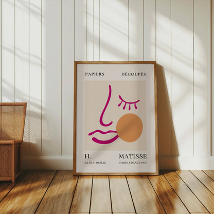 Framed abstract face art inspired by Matisse posters leaning against a white paneled wall in a bright, minimalist room.