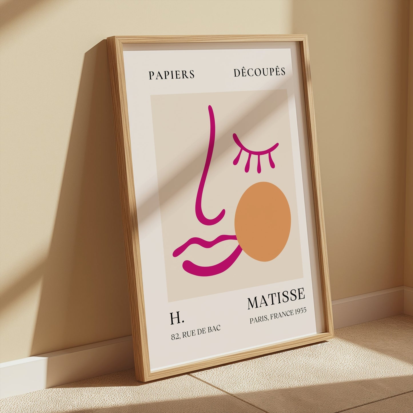 Matisse-inspired abstract face art in a wooden frame, leaning against a beige wall with warm sunlight highlighting its details.