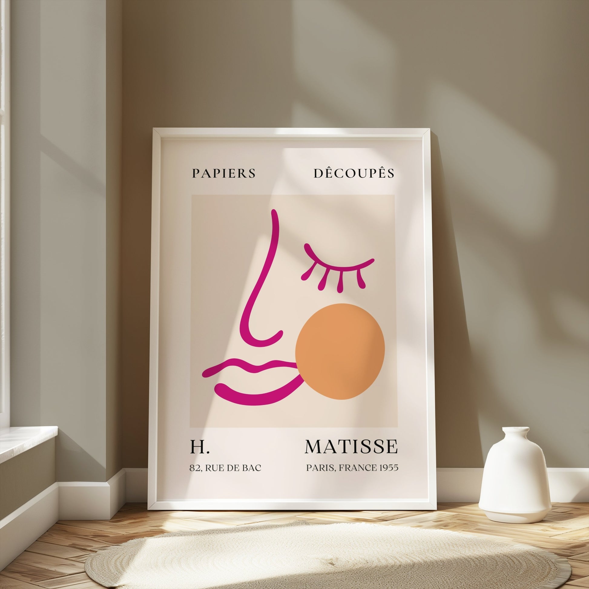 Abstract face art inspired by Matisse posters in a white frame, leaning against a neutral-toned wall in a softly lit room.