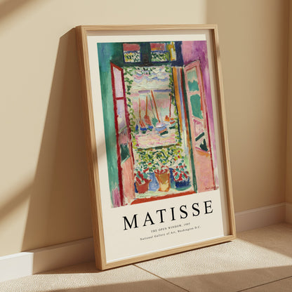 The Open Window by Matisse 1905 framed art print poster leaning against a beige wall, bathed in soft natural light for a warm ambiance.