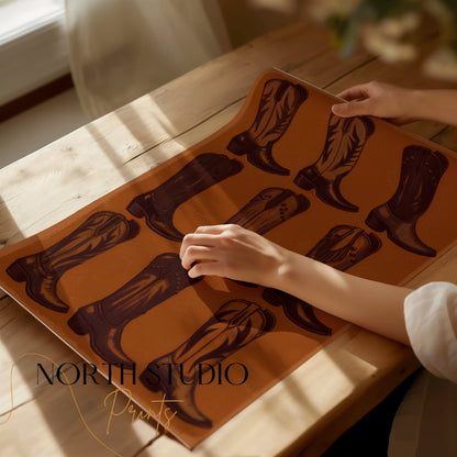Unframed Vintage Cowboy Boots Collection Art Poster being handled on a wooden table with soft natural lighting and a cozy atmosphere.