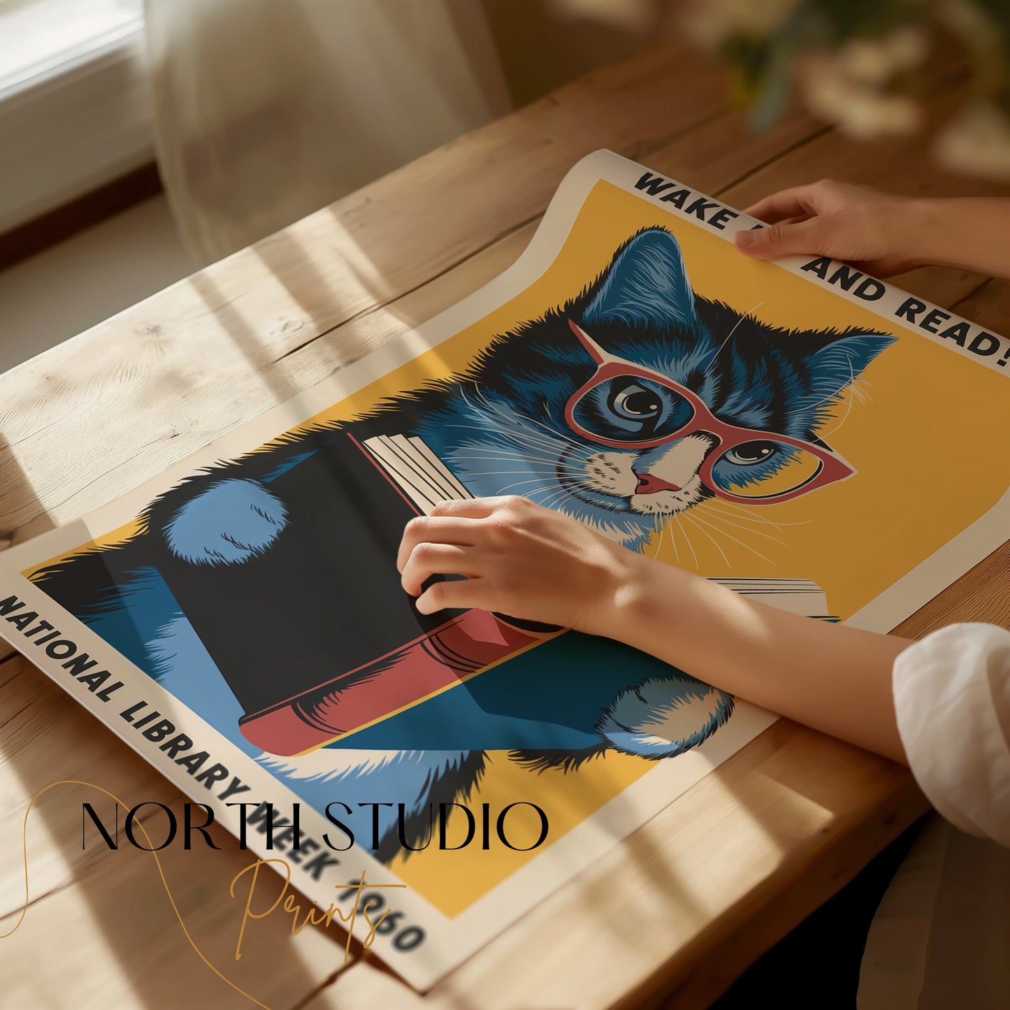 Unframed 'Wake Up and Read!' poster featuring a blue cat with glasses, being handled on a wooden table, showcasing its premium quality.