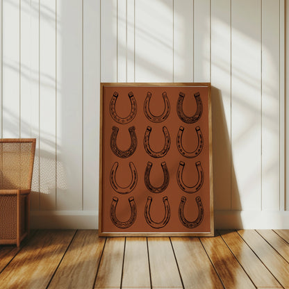Framed artwork displaying a grid of twelve stylized horseshoes on a textured brown background.